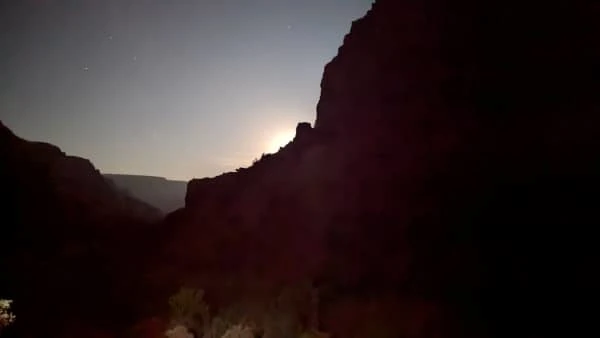 A view from the bottom of the Grand Canyon of the moon setting behind a ridgeline.