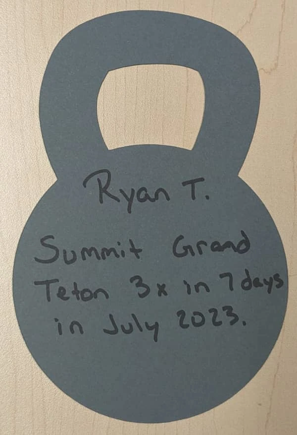 A cutout in the shape of a kettlebell with Coach Ryan's current outcome-oriented goal: Summit Grand Teton three times in a week in July 2023.
