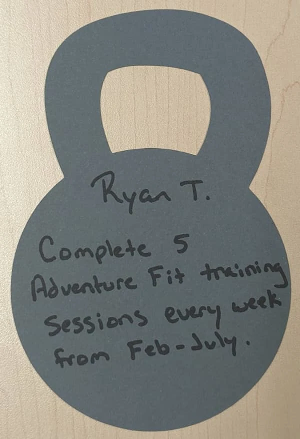 A cutout in the shape of a kettlebell with Coach Ryan's current process-oriented goal: Complete five mountain-focused training sessions every week from February through July.
