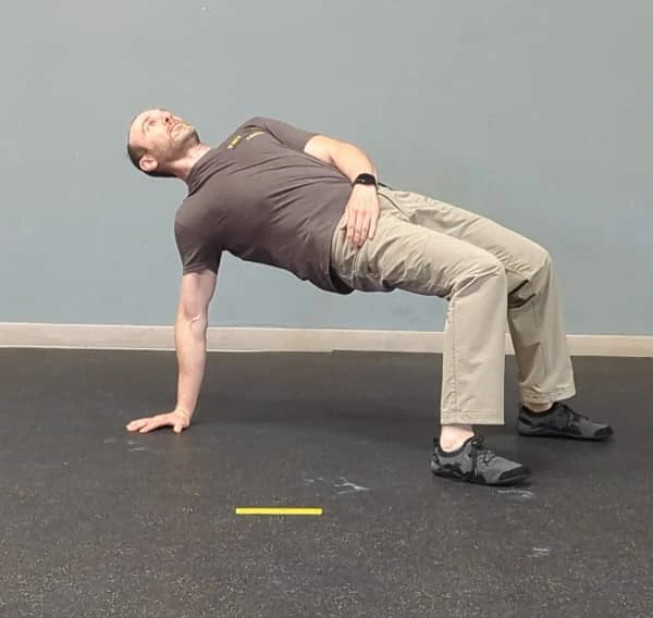 Coach Ryan demonstrates the midpoint position for the T-spine Bridge—just before the final rotation.