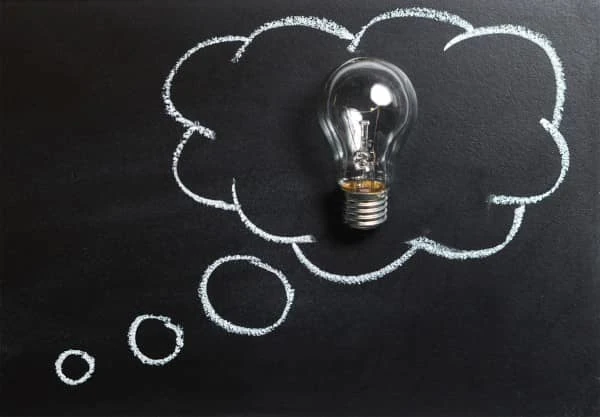A lightbulb resting inside of a chalk-drawn thought bubble.