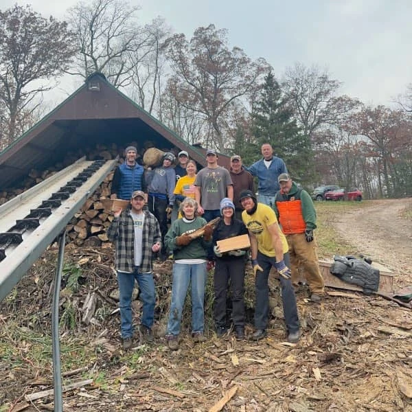 Coach Ryan, family, and friends standing in front of the full woodshed after their annual wood splitting day in 2023.