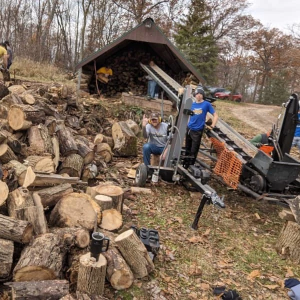 The wood splitting setup at Coach Ryan's dad's place: piles of wood, two hydraulic wood splitters, and a re-purposed hay elevator to move the split pieces to the woodshed.